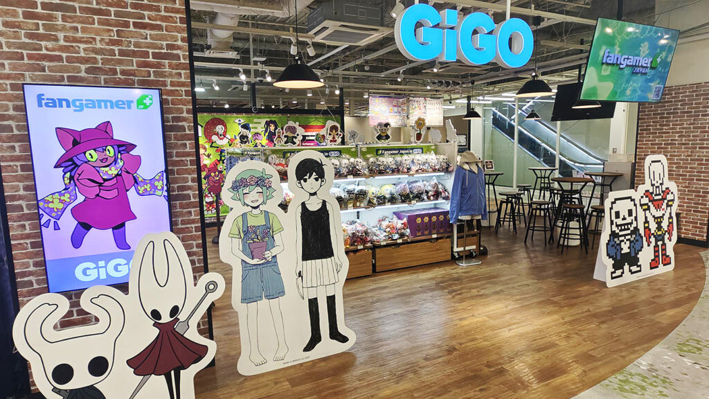 The Fangamer JP storefront at the new GiGO Kyoto. There are large cardboard standees of Hollow Knight, Omori, and Undertale characters. A shelf full of Fangamer's video game merchandise can be seen.