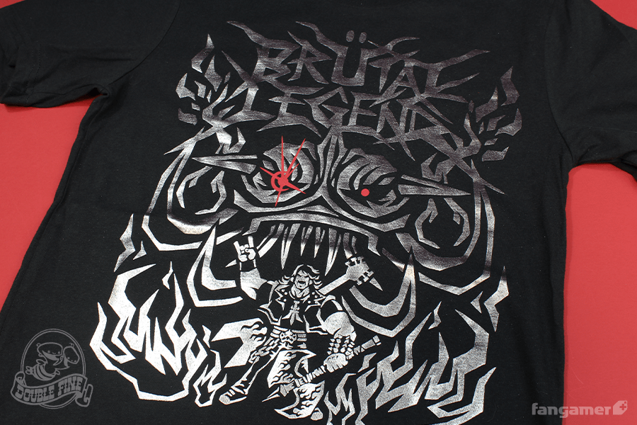 Silver foil-pressed shirt depicting Eddie Riggs doing the metal horns with his hand, standing in front of a large demon skull head. Depicted in big, chunky, jagged lines. The top reads "Brutal Legend."