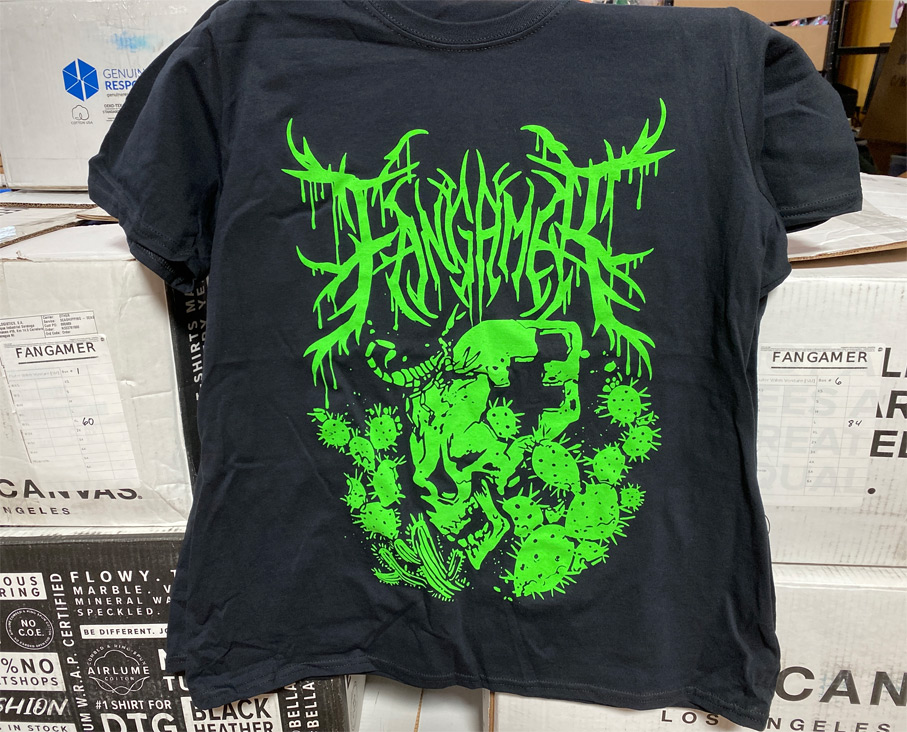 Band-style shirt design of a skull shaped like the Fangamer logo (complete with F-shaped hole), framed with cactuses and a scorpion. Spiky drippy lettering above reads "Fangamer"