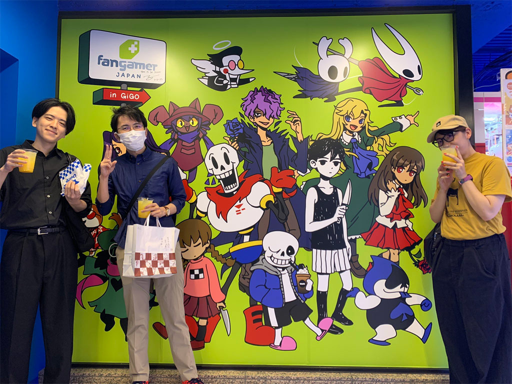 Three people standing in front of the mural, holding drinks and food.